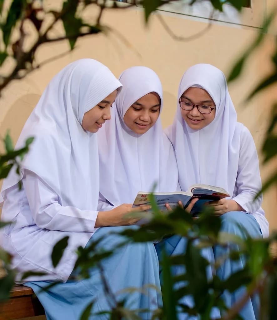 Three schoolgirls in uniform reading a revision book together on a bench